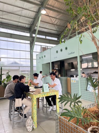 Drei Personen sitzen an einem Tisch in einem modernen, begrünten Café.