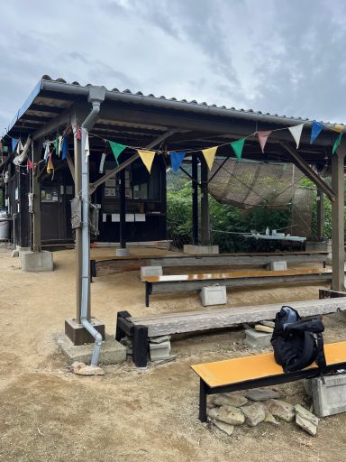 Ruhiger Außenbereich mit bunten Wimpeln und Bänken unter einem überdachten Pavillon.