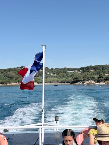 Französische Flagge weht auf einem Boot, Wasser und Küste im Hintergrund.