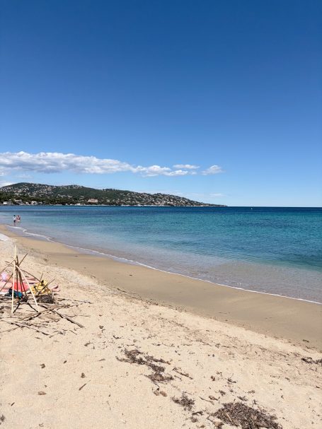 Strand mit feinem Sand, klarem Wasser und blauen Himmel im Hintergrund.
