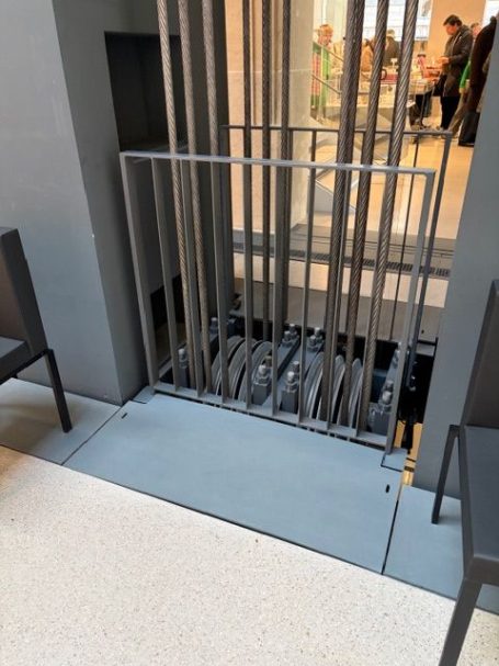 Gitter einer offenen Liftkabine mit Sitzgelegenheiten in der Nähe.