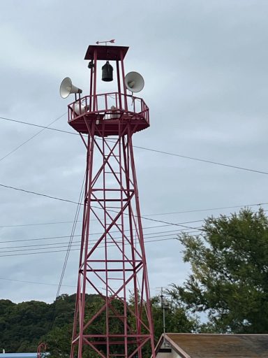 Roter Hochstuhl mit Lautsprechern und Glocke, unter einem bewölkten Himmel.