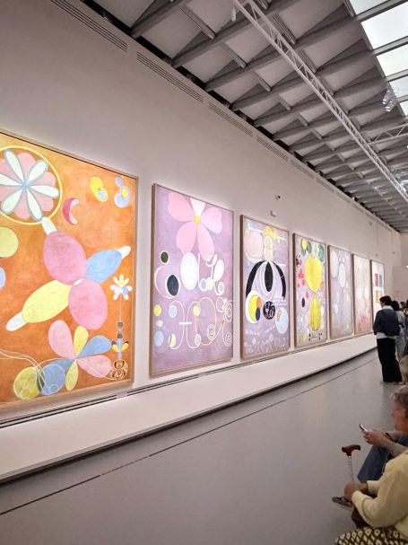 Bunte, abstrakte Blumenmuster auf mehreren großen Kunstwerken in einer Galerie.