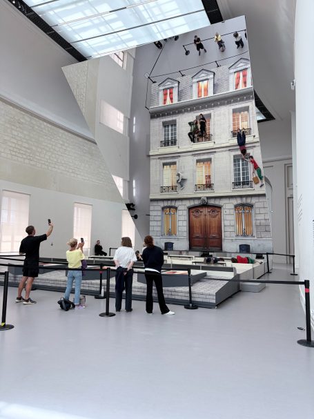Menschen betrachten eine große, eindrucksvolle Wandinstallation eines Hauses in einem Galerie-Raum.