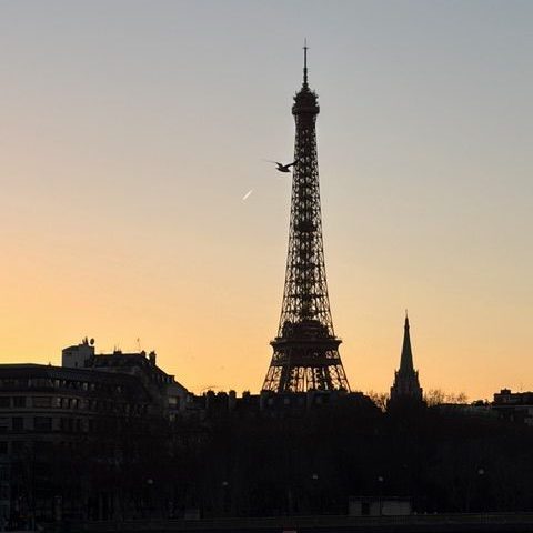 Eiffelturm bei Sonnenuntergang, silhouettiert gegen den orangefarbenen Himmel.