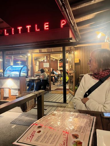 Eine Person sitzt an einem Tisch vor einem Restaurant mit beleuchteter Beschilderung.