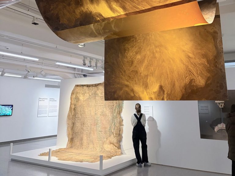 Moderne Kunstinstallation mit goldenen Elementen und einer stehenden Person in einem Ausstellungsraum.