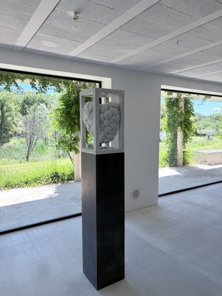 Skulptur in einem modernen Raum, umgeben von großen Fenstern und grünem Ausblick.
