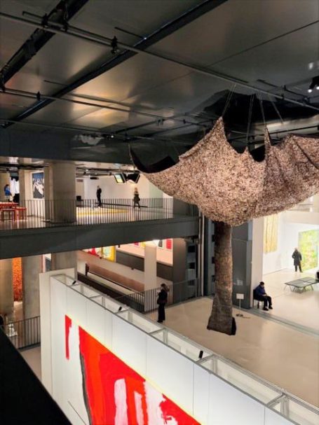 Große, hängende Installation in einem modernen Ausstellungsraum mit farbigen Gemälden.