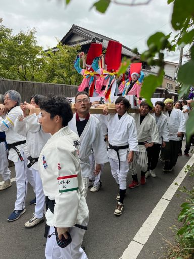 Menschen in traditioneller Kleidung tragen einen festlichen Umzug mit bunten Elementen.