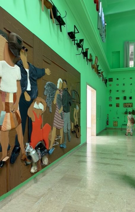 Bunte Wandmalerei mit stilisierten Figuren in einem hellgrünen Raum.