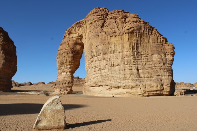 Felsbogen in der Wüste mit goldenem Sand und klarem blauen Himmel.