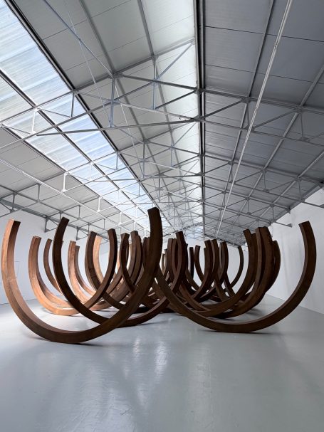Moderne Skulpturen aus gebogenen Holzstücken in einem hellen Ausstellungsraum.