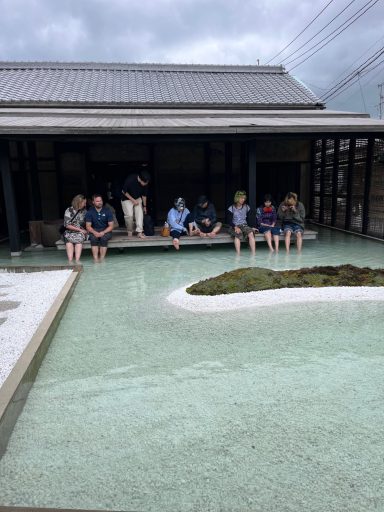 Menschen sitzen am Rand eines Wassergartens vor einem modernen Gebäude.
