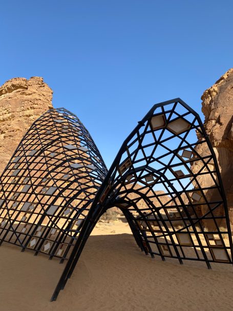 Moderne, geschwungene Struktur aus schwarzem Metall in einer Wüstenlandschaft.