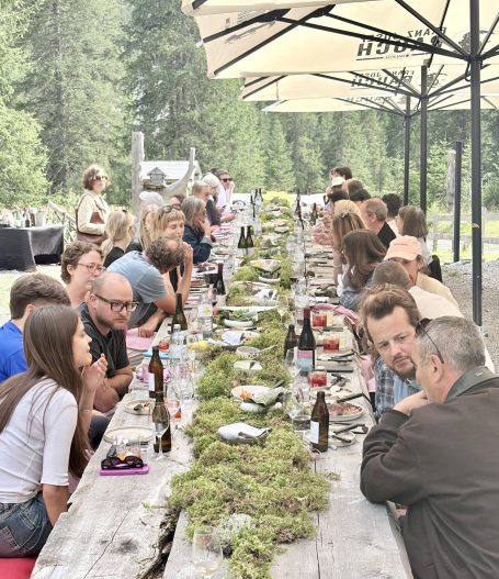 langer Tisch mit Moos in der Mitte rechts und links Personen die essen 