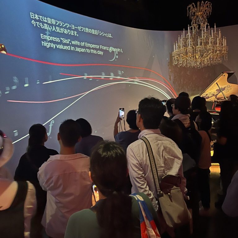 Menschen stehen vor einer Präsentation mit farbigen Grafiken und einem Kronleuchter im Hintergrund.