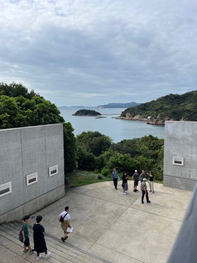 Blick auf die Küste mit einer Gruppe von Menschen und bewaldeten Hügeln im Hintergrund.