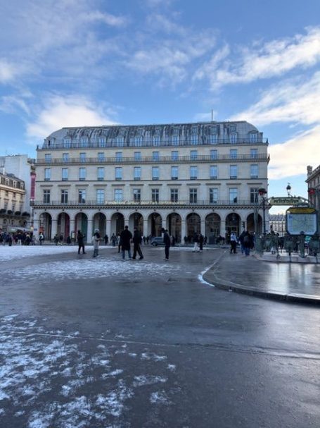 Historisches Gebäude mit Säulen unter blauem Himmel und Menschen auf einem Platz.