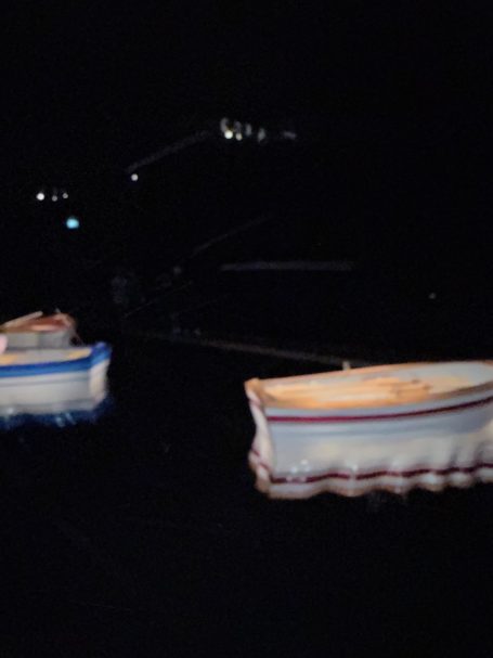 Zwei Boote schwimmen nachts auf ruhigem Wasser, schwach beleuchtet.
