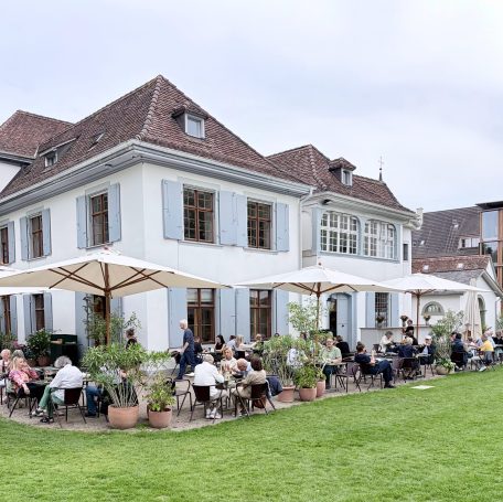 Weißes Haus mit rotem Dach, Terrasse mit Gästen unter Schirmen