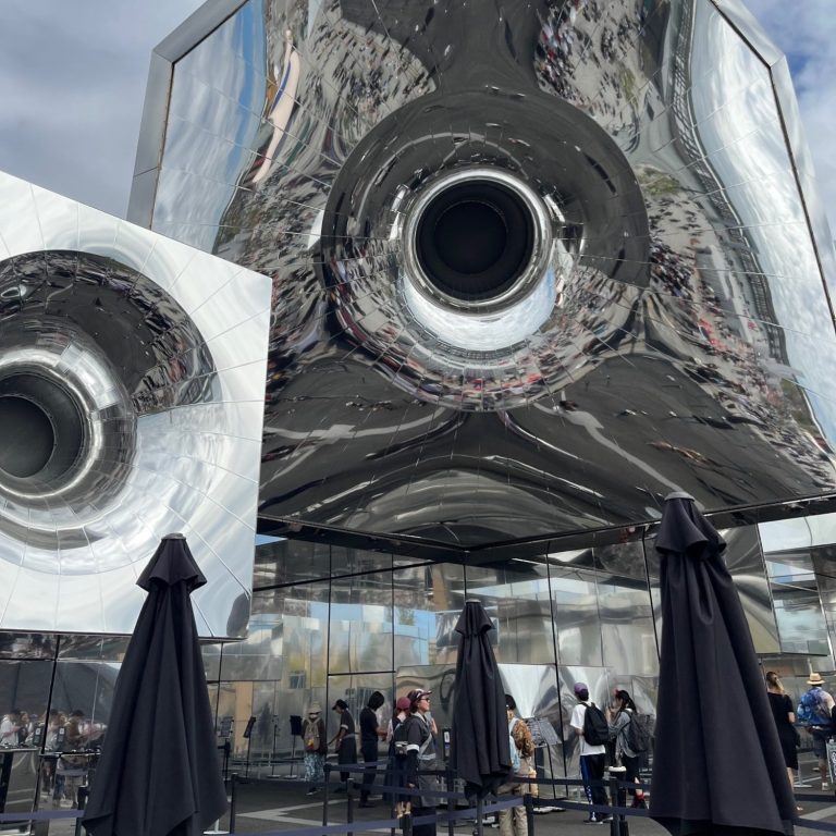 Reflektierendes Gebäude mit schwarzen Sonnenschirmen im Vordergrund.