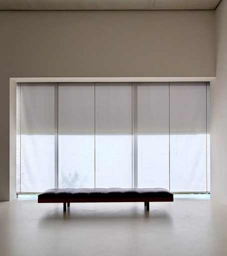 Blick auf Fensterfront mit Rollos herbagezogen und flacher Sitzbank mit Leder