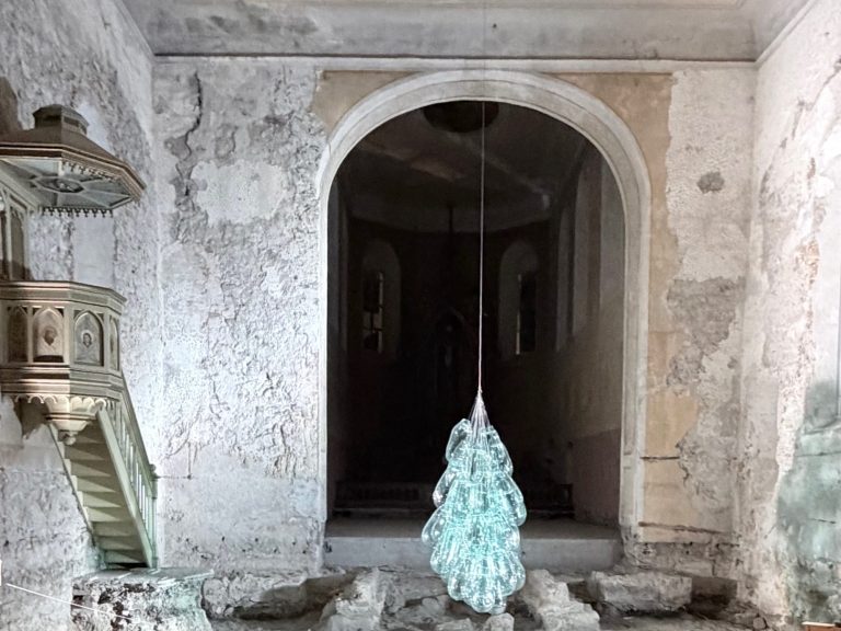 Kunstwerk aus grünen Glasfragmenten hängt in einer Kirche.