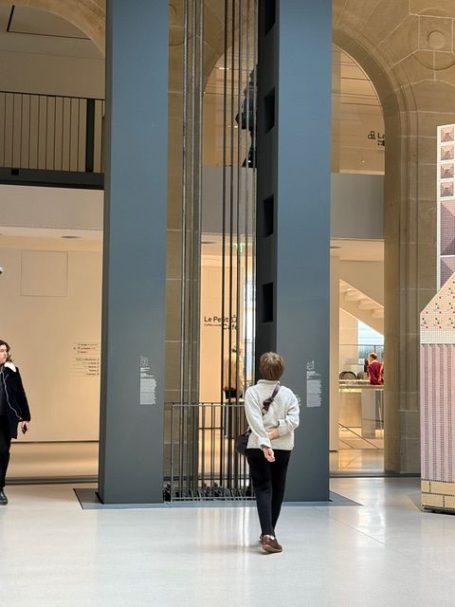 Person steht im Foyer eines modernen Gebäudes neben einem Aufzug.