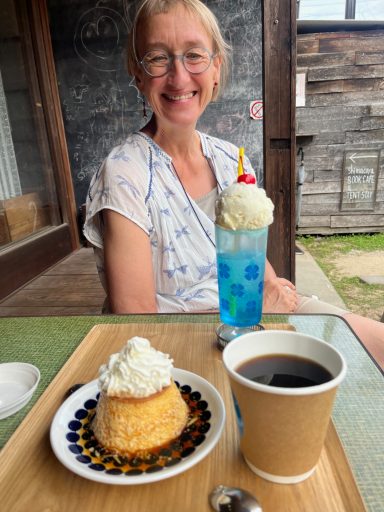 Eine Person sitzt mit einem Dessert und einem Getränk am Tisch im Freien.