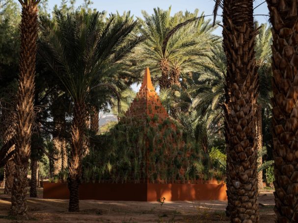 Ein orangefarbenes Gebäude, umgeben von hohen Palmen in einer grünen Landschaft.
