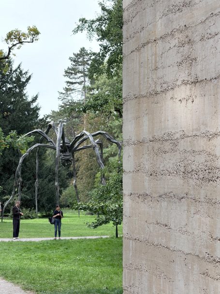 Metallspinne im Park, ein angeschnittener baum und eine Wand des Gebäudes